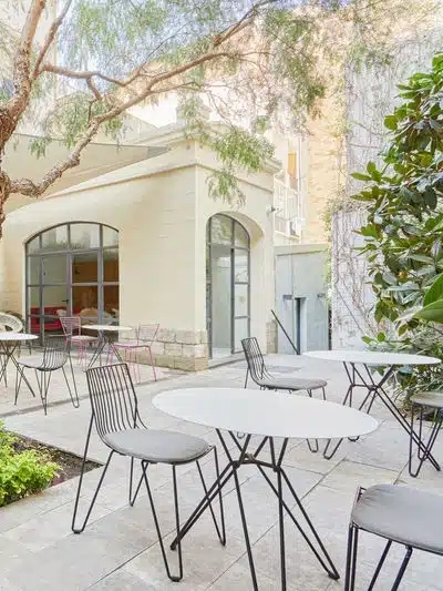 Una terraza en Barcelona para evento en la ciudad o fuera de ella. Mesas y sillas en una terraza al aire libre con arboles y plantas.
